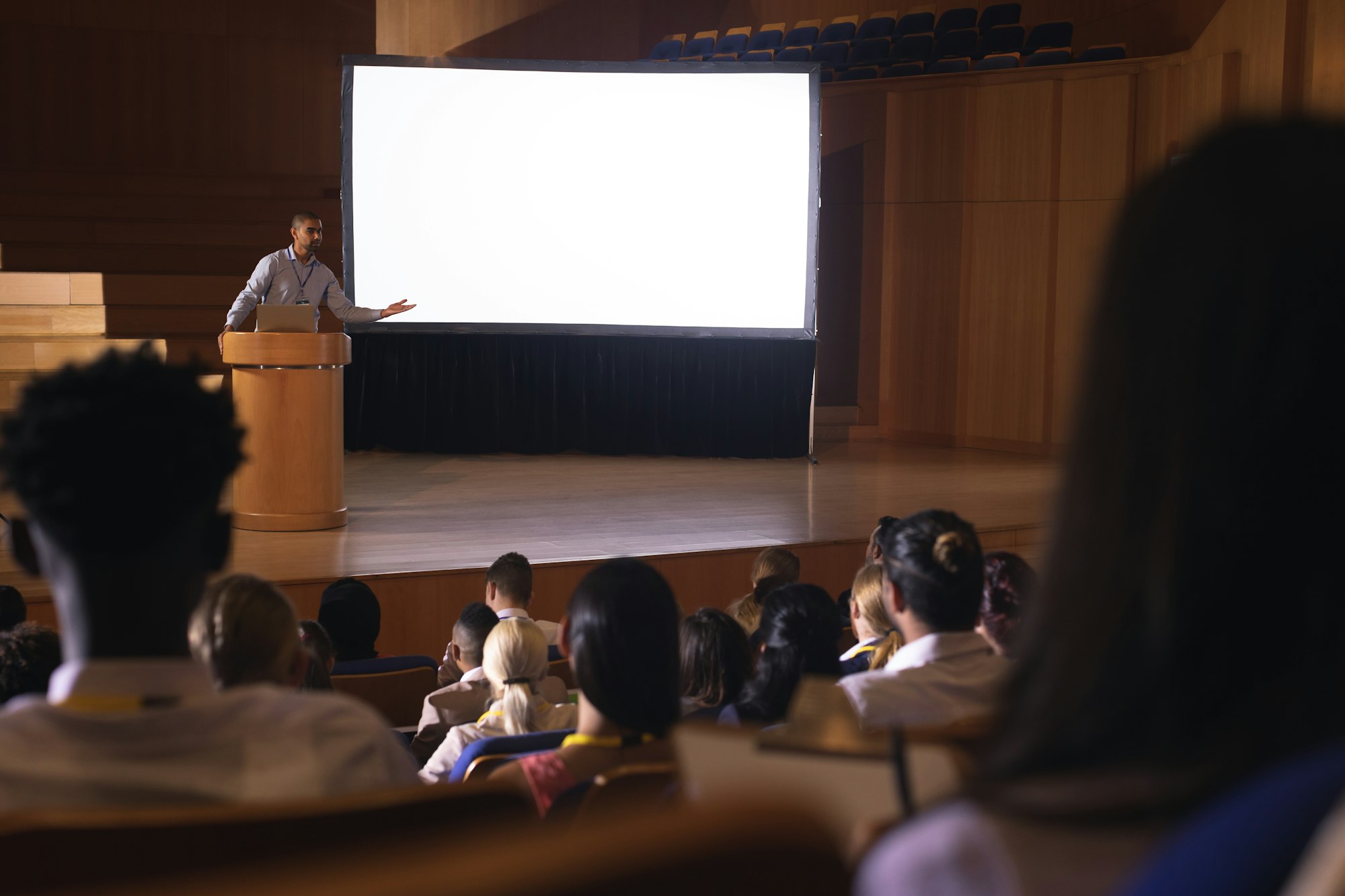 Man standing at a podium giving a presentation in an auditorium at a dental conference.