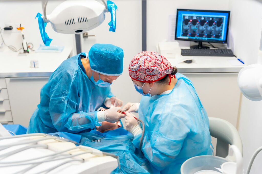 Female dentists in blue scrubs performing a complicated operation on a female patient, sucking blood